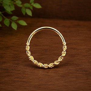 May include: A circular gold hoop ring featuring a twisted rope-like texture along the bottom half of the band. The jewelry piece has a smooth, polished finish on the upper section and a hinged closure mechanism visible at the top of the hoop.