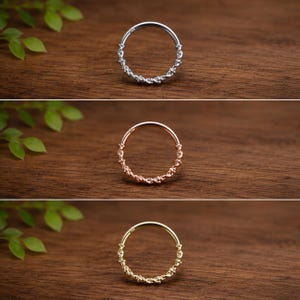 May include: A set of three circular hoop rings, each featuring a twisted rope-like texture along the bottom half and a smooth segment at the top. The rings are presented in silver, rose gold, and yellow gold tones, showcasing a hinged design.