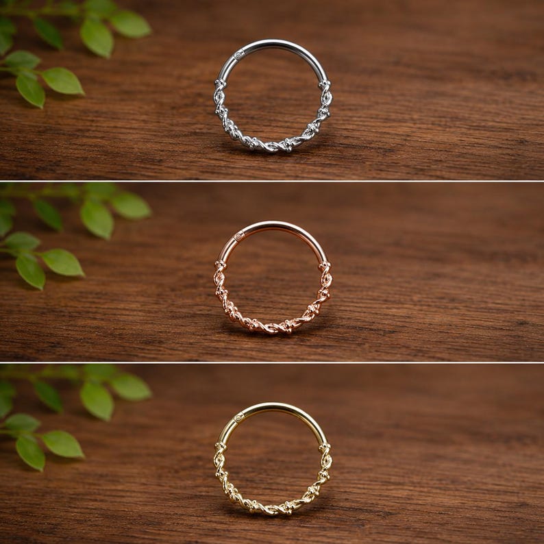 May include: A set of three circular hoop rings, each featuring a twisted rope-like texture along the bottom half and a smooth segment at the top. The rings are presented in silver, rose gold, and yellow gold tones, showcasing a hinged design.