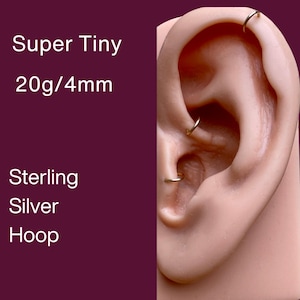 May include: Close-up of an ear with several small, gold-coloured hoop earrings. The text on the left reads "Super Tiny 20g/4mm Sterling Silver Hoop."