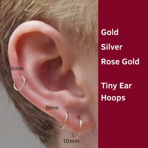 May include: An ear with three small gold hoop earrings, measuring 6mm, 8mm, and 10mm. The image includes the text "Gold, Silver, Rose Gold, Tiny Ear Hoops" on a maroon background.