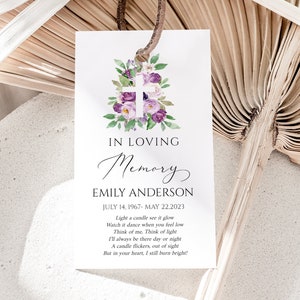 May include: A white memorial card featuring a purple floral design and a white cross. The text reads "In Loving Memory Emily Anderson July 14, 1967 - May 22, 2023" and includes a poem about a candle.