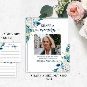 May include: A white sign with blue floral accents and a photo of a woman. The sign says "Share a memory" and "Please take a card and share a memory of our beloved Ashley Anderson".
