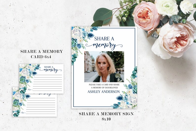 May include: A white sign with blue floral accents and a photo of a woman. The sign says "Share a memory" and "Please take a card and share a memory of our beloved Ashley Anderson".