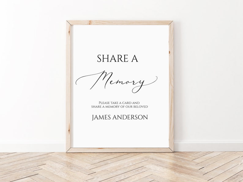 May include: A white sign with a black frame, the text "SHARE A Memory" in a cursive font, and the text "PLEASE TAKE A CARD AND SHARE A MEMORY OF OUR BELOVED JAMES ANDERSON" in a sans-serif font.