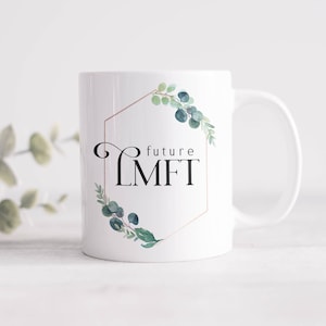 May include: White ceramic mug with a gold hexagonal frame and green watercolor foliage. The text "future LMFT" is inside the frame.