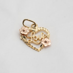 May include: Gold heart-shaped pendant with the word "LOVE" inscribed inside. The pendant is decorated with two small pink flowers.