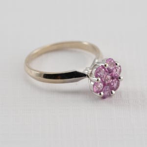 May include: A gold and silver ring with a cluster of pink gemstones set in the center.