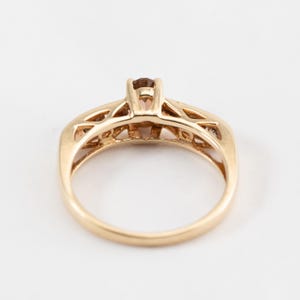 Puede incluir: Un anillo de oro con una piedra preciosa marr&oacute;n en el centro y piedras preciosas m&aacute;s peque&ntilde;as en la banda.