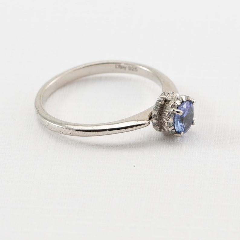 May include: A silver ring with a blue gemstone set in a silver crown. The ring is marked "925" on the inside band.