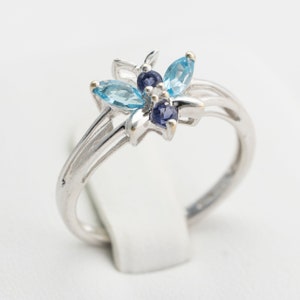 Pu&ograve; includere: Un anello d'argento con un design floreale con pietre preziose blu e viola.