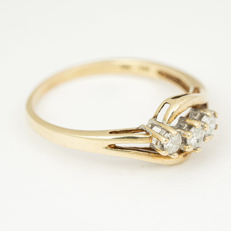 May include: A gold ring with three small, round diamonds set in a cluster. The band is a simple, polished gold, and the diamonds are set in a white metal. The ring is shown on a white background.