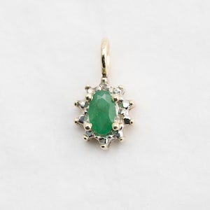 May include: A gold pendant featuring a green emerald gemstone surrounded by a halo of smaller diamonds.