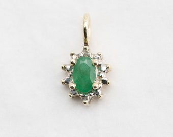 May include: A gold pendant featuring a green emerald gemstone surrounded by a halo of smaller diamonds.