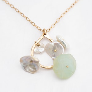 May include: A gold necklace with a delicate chain and a pendant featuring a circular hoop with multiple white and green gemstone accents.