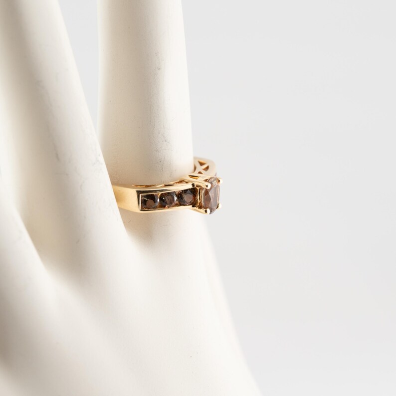 Puede incluir: Un anillo de oro con una piedra preciosa marr&oacute;n y piedras marrones m&aacute;s peque&ntilde;as engastadas en la banda.