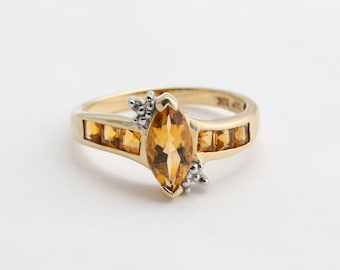 May include: A gold ring featuring a marquise-shaped topaz gemstone surrounded by smaller diamonds. The band of the ring is set with smaller topaz gemstones.