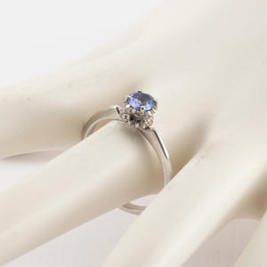 May include: A silver ring with a blue gemstone set in a crown of smaller diamonds.