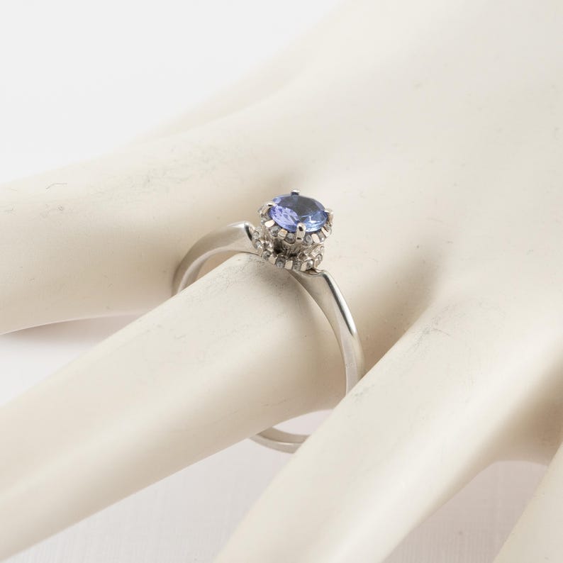 May include: A silver ring with a blue gemstone set in a crown of smaller diamonds.