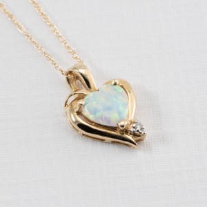 May include: A gold heart-shaped pendant necklace with a white opal gemstone and a small diamond accent.