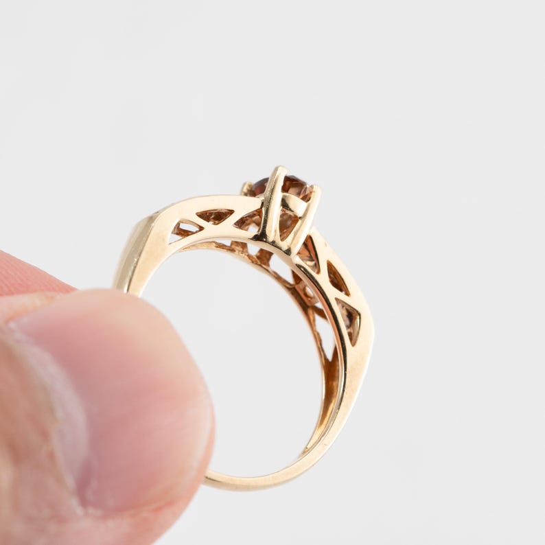 Puede incluir: Un anillo de oro con una piedra preciosa marr&oacute;n engastada en un dise&ntilde;o delicado e intrincado.
