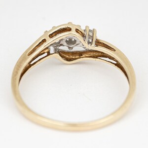 May include: A gold ring with a central diamond and two smaller diamonds on either side. The ring has a split shank design and a polished finish. The ring is set against a white background.