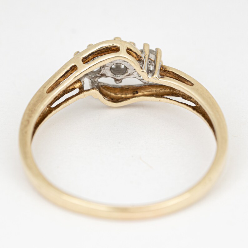 May include: A gold ring with a central diamond and two smaller diamonds on either side. The ring has a split shank design and a polished finish. The ring is set against a white background.