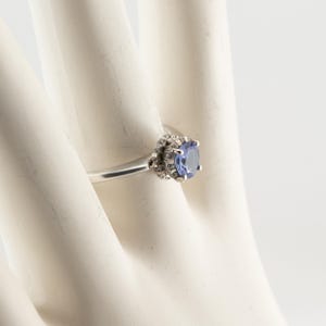 May include: A silver ring with a blue gemstone surrounded by smaller white gemstones.