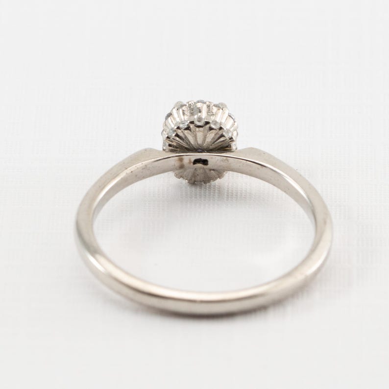 May include: A silver ring with a round, clear stone surrounded by smaller stones.