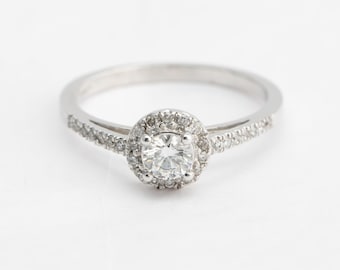 May include: A silver ring with a round, clear diamond center stone surrounded by smaller diamonds. The band is also set with small diamonds.