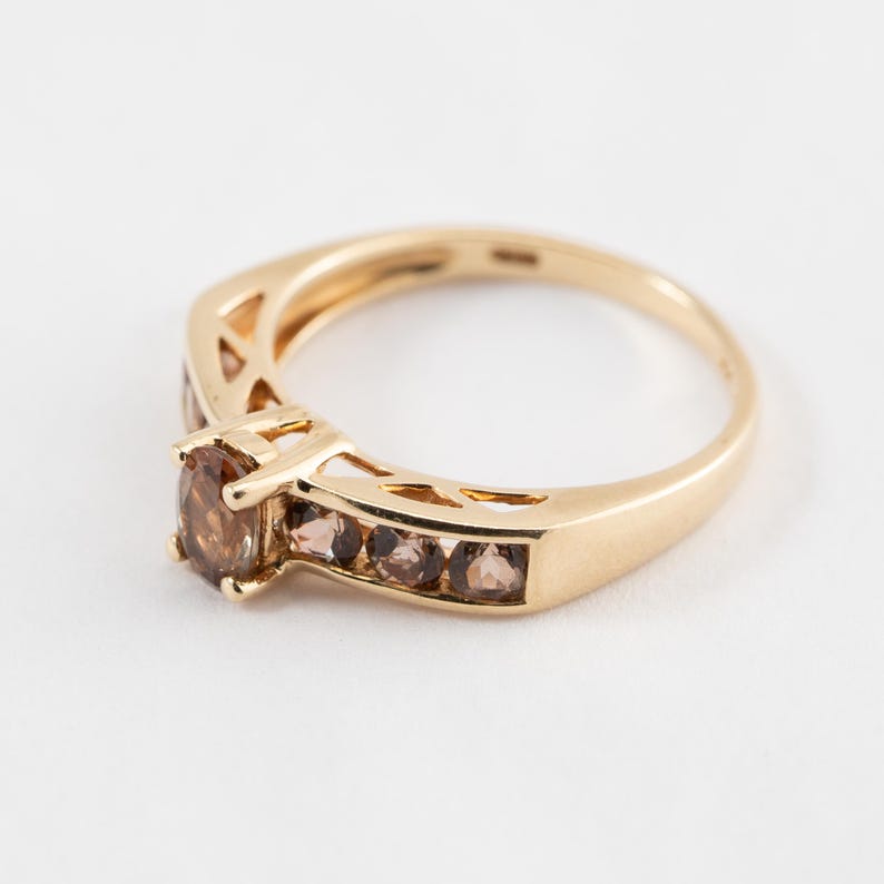 Puede incluir: Un anillo de oro con una sola piedra preciosa redonda marr&oacute;n y una banda de piedras preciosas marrones m&aacute;s peque&ntilde;as.