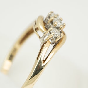 May include: A gold ring with a cluster of three small diamonds. The ring has a split shank design and a white metal setting for the diamonds. The ring is set against a white background.