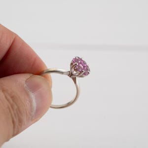 May include: A silver ring with a cluster of pink gemstones set in the center.