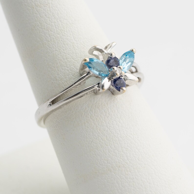 Pu&ograve; includere: Un anello d'argento con un gruppo di pietre preziose blu e viola incastonate in un design floreale.