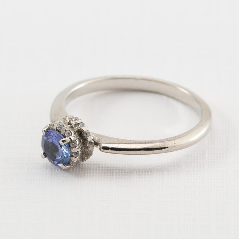 May include: A silver ring with a blue gemstone surrounded by smaller white gemstones.