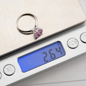 May include: A silver ring with a pink gemstone is on a digital scale that reads 2.64 grams.