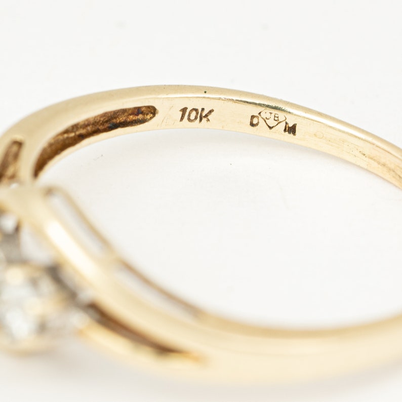 May include: A gold ring with a cluster of small, clear stones. The ring band is a smooth, polished gold. The ring is stamped with "10K" and other markings.