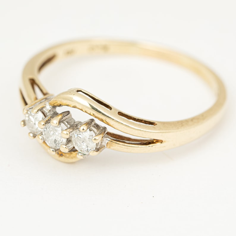 May include: A gold ring with three clear diamonds set in a row. The ring has a delicate, curved design with a polished finish. The diamonds are round and sparkle against the gold band. A classic piece of jewelry.