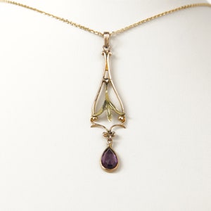May include: A gold pendant necklace with a purple gemstone drop. The pendant features an intricate design with a leaf motif.