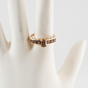 Puede incluir: Un anillo de oro con un solo diamante marr&oacute;n en el centro y una banda de diamantes marrones m&aacute;s peque&ntilde;os.