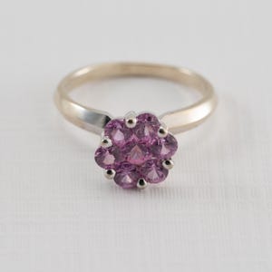 May include: A silver ring with a cluster of pink gemstones set in the center.