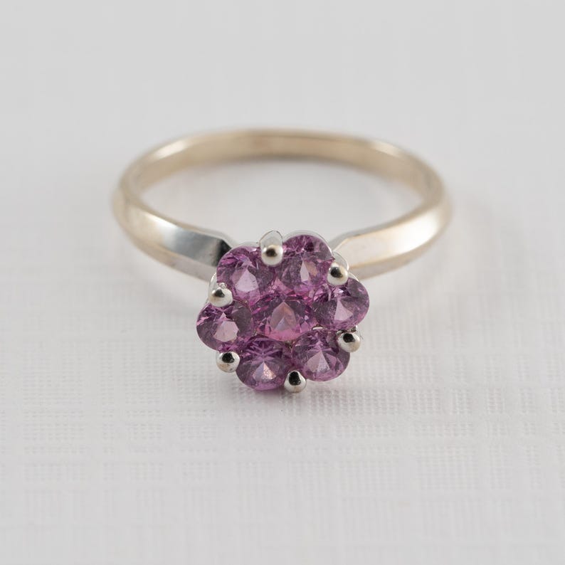 May include: A silver ring with a cluster of pink gemstones set in the center.