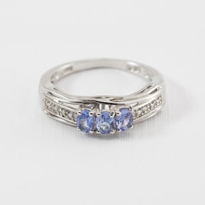 May include: A silver ring with three blue gemstones and a row of small diamonds on each side.
