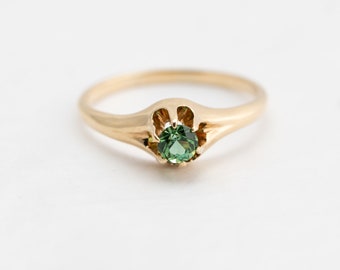 May include: A gold ring with a green gemstone set in a flower-shaped setting.