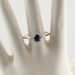 May include: A silver ring with a blue gemstone set in a crown-shaped halo.