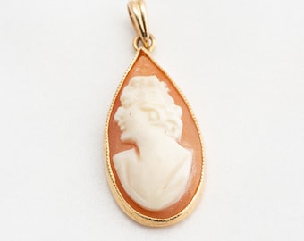 May include: A gold pendant with a cameo of a woman's profile in a teardrop shape. The cameo is made of white shell and is set in a gold frame.