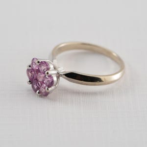 May include: A silver ring with a cluster of pink gemstones set in the center.