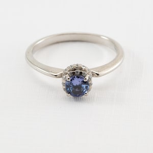 May include: A silver ring with a blue gemstone surrounded by smaller white gemstones.