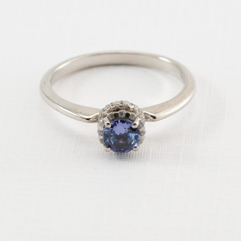 May include: A silver ring with a blue gemstone surrounded by smaller white gemstones.