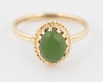 May include: A gold ring with a green oval gemstone set in a rope-like design.